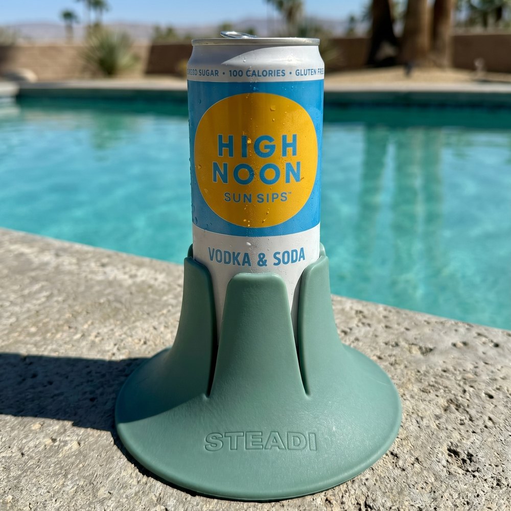 A slim can standing in a sage Steadi on wet stone coping, with pool water behind it.